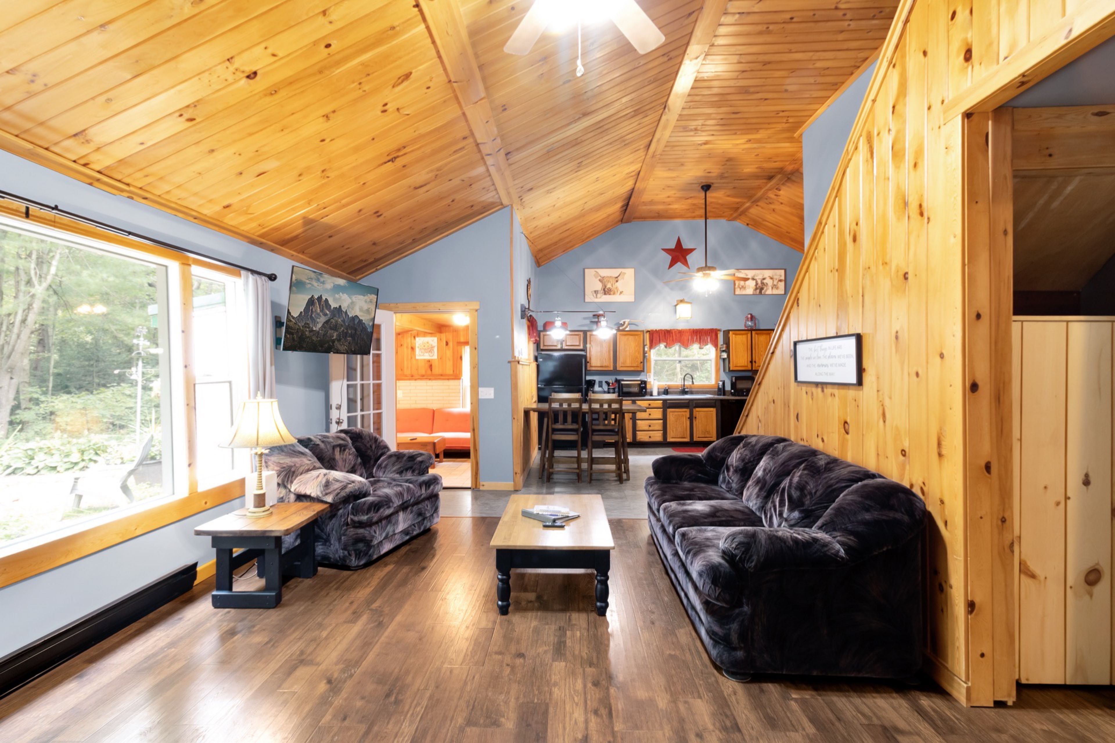 A cozy cabin interior with a dining area, two sofas, and a kitchen.