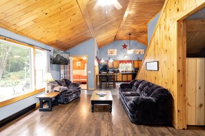 A cozy cabin interior with a dining area, two sofas, and a kitchen.