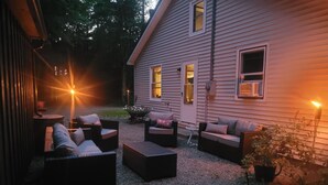An outdoor seating area with wicker furniture and a small table, surrounded by a gravel path and a house with windows. - A short walk to a private beach for swimming boating or fishing  (Arcade)