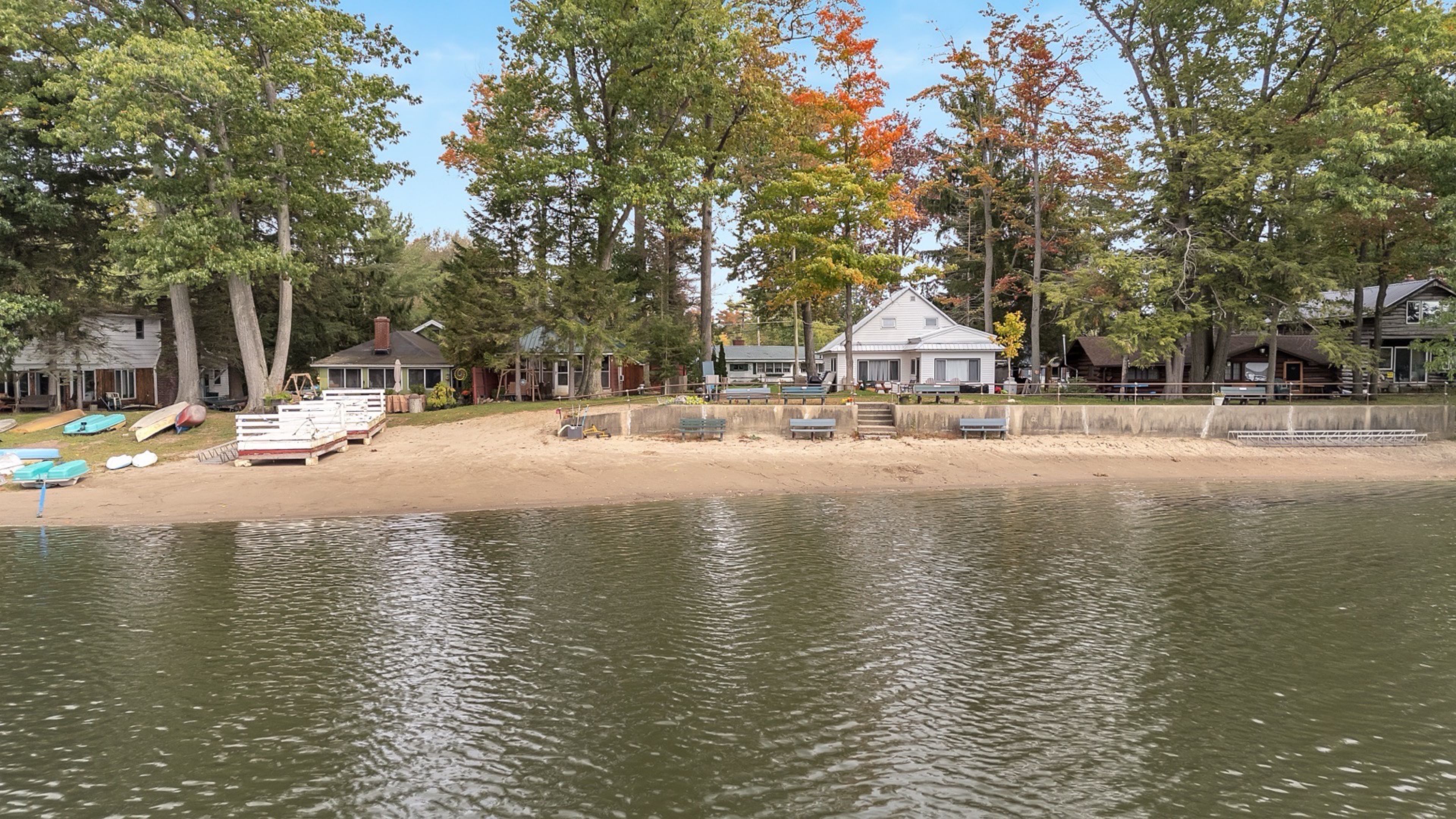 A lakeside property with a sandy beach, docked boats, and a house with a porch.