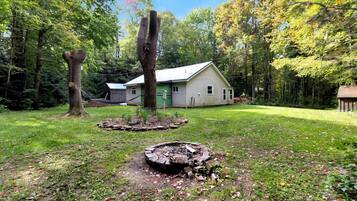 A house with a green roof, surrounded by a wooded area with tall trees and a well-maintained lawn.