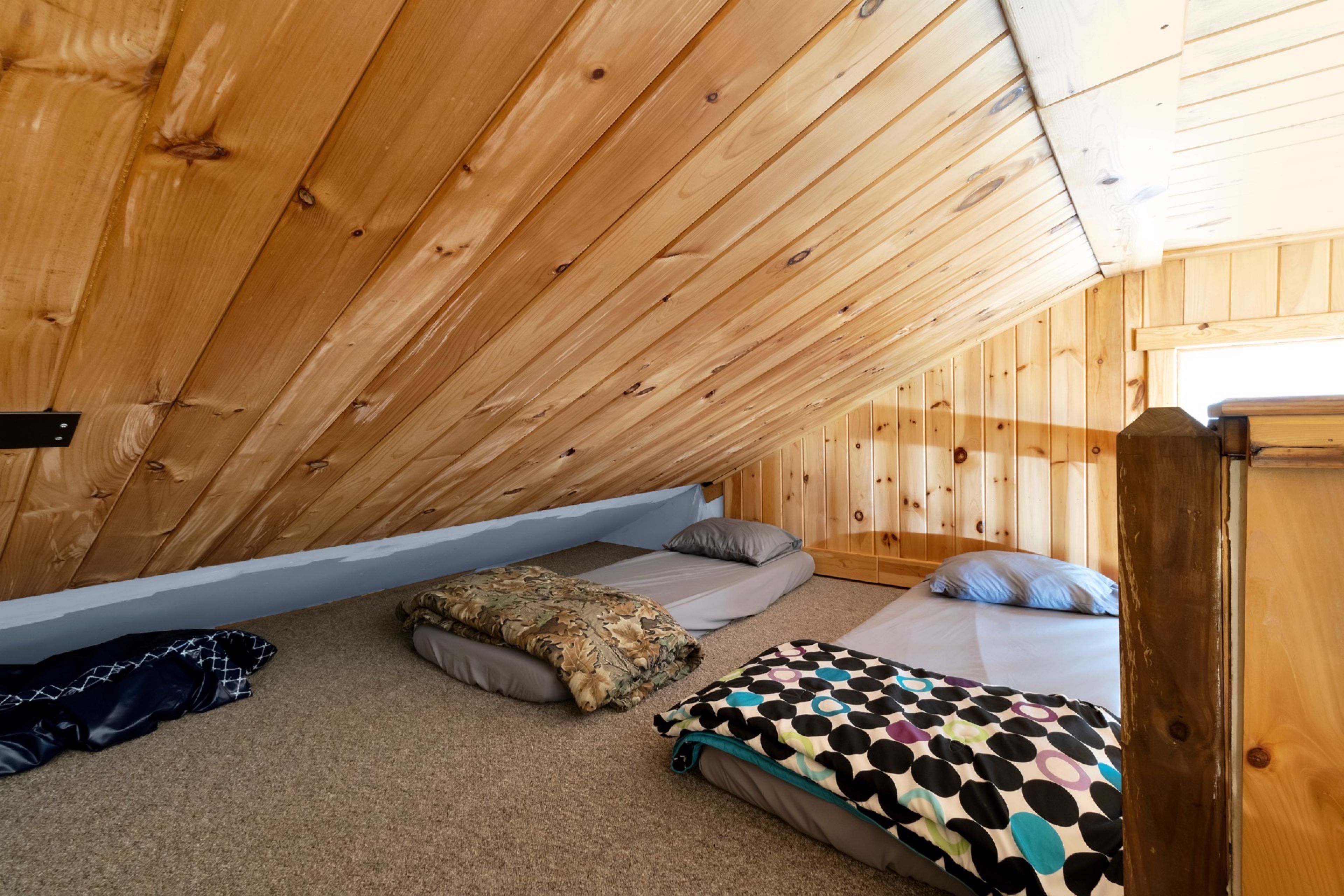 A cozy attic bedroom with wooden walls and sloped ceilings, featuring two beds with various bedding.