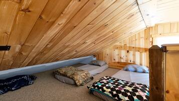 A cozy attic bedroom with wooden walls and sloped ceilings, featuring two beds with various bedding.