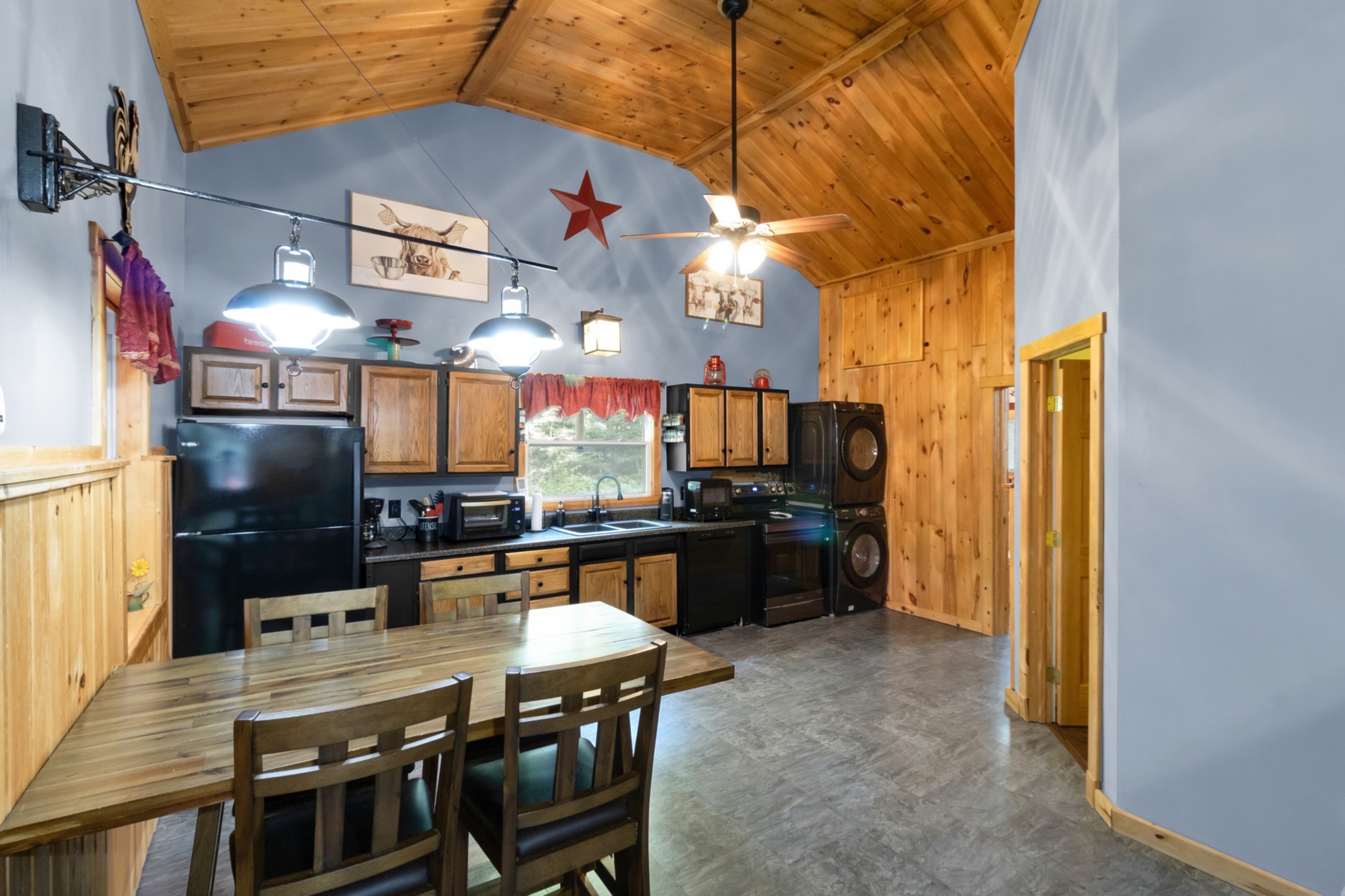 A kitchen with wooden cabinets, a dining table with chairs, a ceiling fan, and various kitchen appliances.