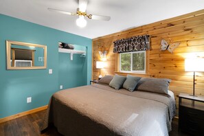 A bedroom with a bed, a ceiling fan, a window with curtains, a wall-mounted shelf, and a butterfly decoration. - Escape to this all season peaceful getaway. (Arcade)