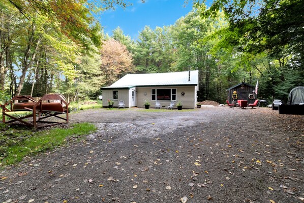 A cabin with a gravel driveway, surrounded by trees. - Escape to this all season peaceful getaway. (Arcade)