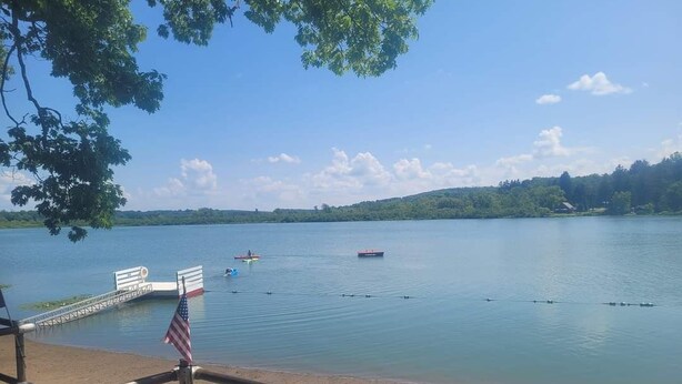 A lakeside view with a dock, a bench, and an American flag. - A short walk to a private beach for swimming boating or fishing  (Arcade)
