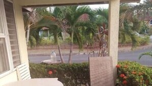 Ein überdachter Außenbereich mit Tisch und Bänken, umgeben von viel Grün und Blick auf eine Straße.