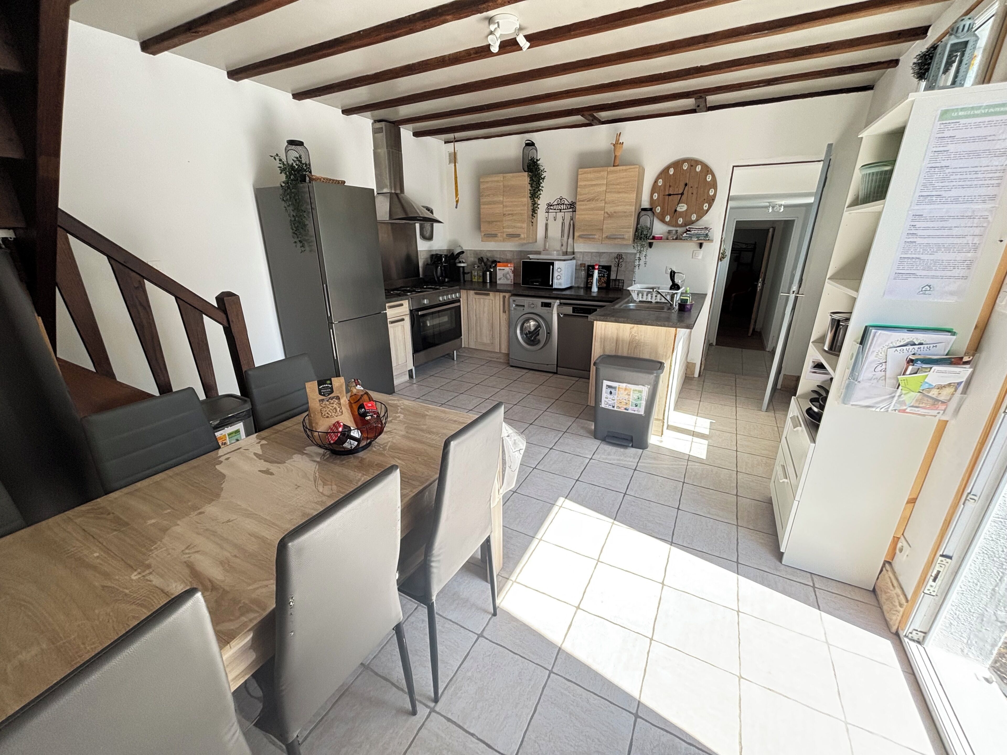 A modern kitchen with a dining area, wooden cabinets, a built-in oven, and a trash bin.