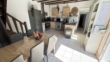 A modern kitchen with a dining area, wooden cabinets, a built-in oven, and a trash bin.