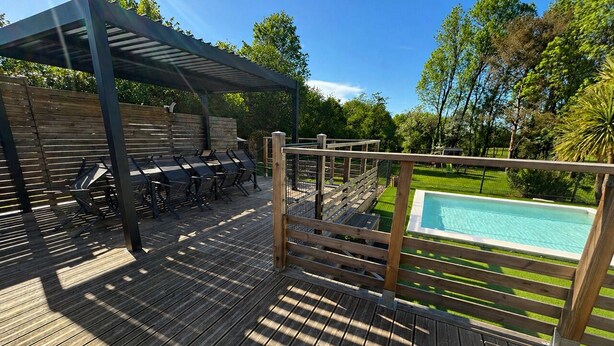 Eine Holzterrasse mit Pool, einer überdachten Lounge und einem Zaun.