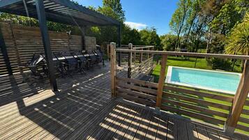 A wooden deck with a pool, a covered seating area, and a fence.