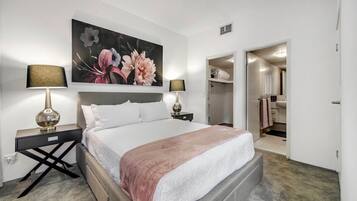 Una habitación de hotel con una cama grande, dos mesitas de noche con lámparas, una obra de arte floral grande en la pared y un vestidor.