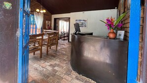 A reception area with a wooden desk, chairs, a computer, and a potted plant. - POUSADA SAO JOSE (Chapada dos Guimarães)