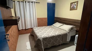 A bedroom with a bed, a ceiling fan, an air conditioning unit, a blue door, and a small table.