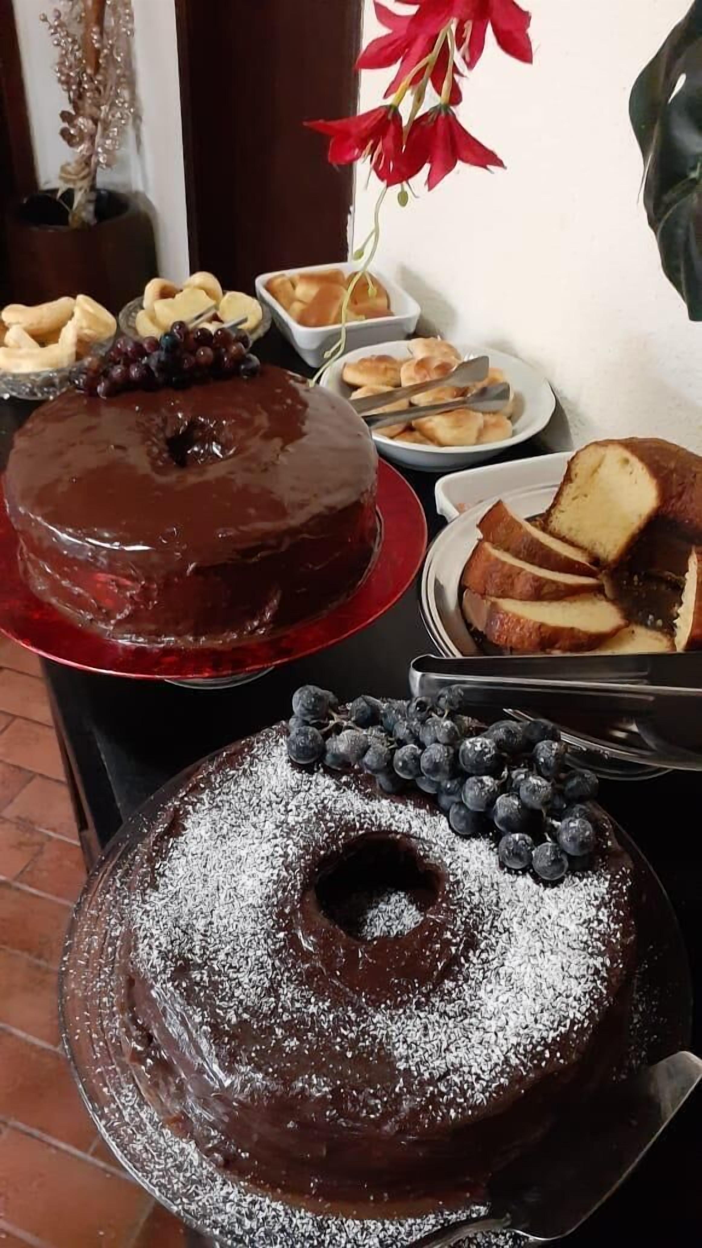 A dessert table with a chocolate bundt cake, a chocolate-covered cake with blueberries, and various pastries.