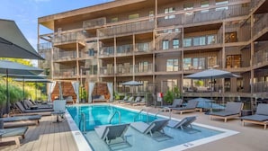 Un edificio de varios pisos con piscina en la azotea, zona de estar al aire libre y terraza de madera.