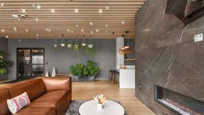 A modern interior with a leather sofa, a round coffee table, hanging plants, a fireplace, and a kitchen area. - NashVybe PH Condo| Broadway & Gulch| Pool, Parking (Nashville)