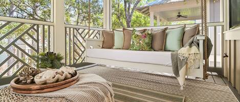 A covered porch with a cushioned seating area, a woven rug, and a rustic wooden tray with decorative items.