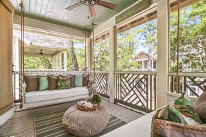 A covered porch with a swing, a cushioned bench, a woven ottoman, and a view of the outdoors. - 5BR WaterColor | Cart + Bikes | Luxe Kings + Bunks | 2026 10–15% Off 5–7+ Nights (Santa Rosa Beach)