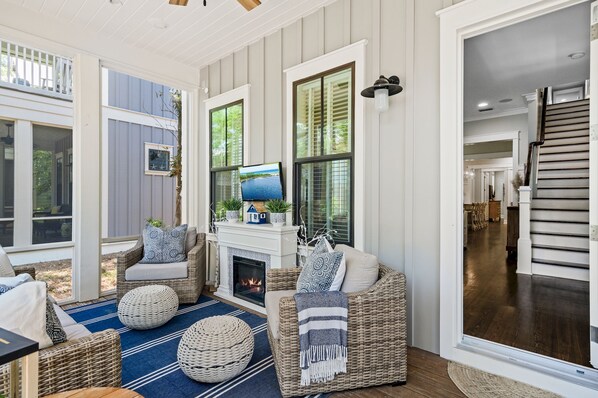 A cozy living room with wicker furniture, a fireplace, and large windows. - WaterColor 4BR w/ Luxe Lounge | 3 King Suites + Private Bunk | Cart + Beach Club (Santa Rosa Beach)