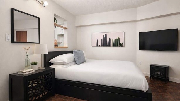 Un dormitorio moderno con cama, mesitas de noche, televisor y obras de arte en las paredes.