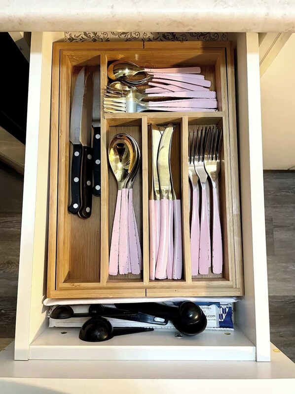 A drawer with utensils, including knives, spoons, and forks, neatly organized.