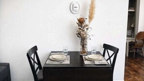 Una mesa de comedor con dos sillas, un jarrón con plantas secas y un dispositivo montado en la pared.