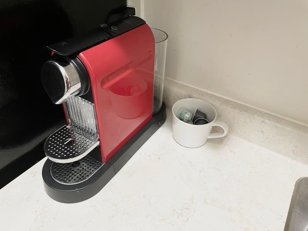 A red coffee machine with a transparent water container and a white mug on a countertop.