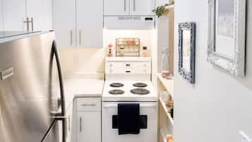 Una cocina compacta con refrigerador de acero inoxidable, estufa blanca y gabinetes blancos, además de una toalla negra.