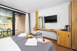 Una habitación de hotel moderna con una cama, un televisor, un armario de madera y un balcón con vistas a casas.