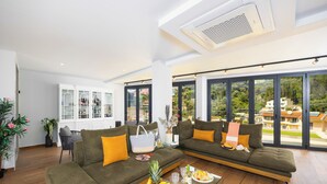 A modern living room with a large sofa, a glass coffee table with fruit and drinks, and a view of a green landscape through large windows. - Nobile Hotel (Corfu)
