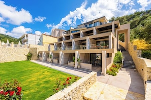 Un edificio moderno de varios pisos con fachada de piedra, un césped cuidado y una escalera que conduce a los niveles superiores.
