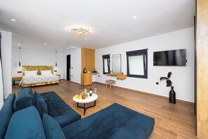 A modern hotel room with a large bed, a sofa, a small table with fruit and wine, and a TV mounted on the wall. - Nobile Hotel (Corfu)