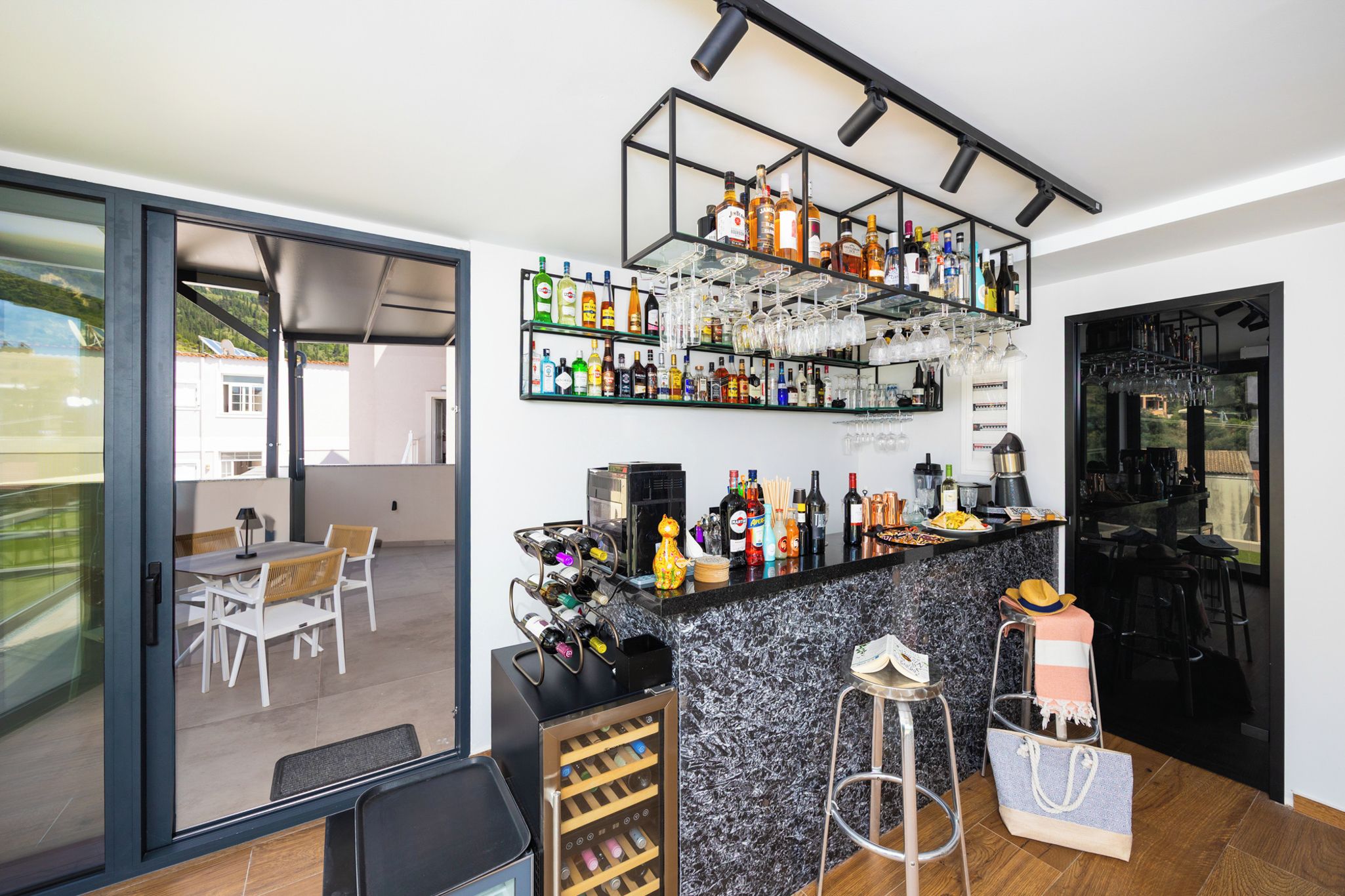 A modern kitchen with a bar area, featuring a wine rack, shelves with bottles, and a countertop with various kitchen appliances.