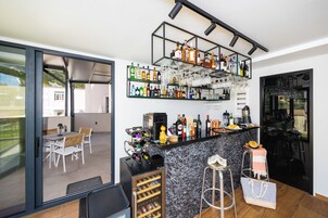 A modern kitchen with a bar area, featuring a wine rack, shelves with bottles, and a countertop with various kitchen appliances.