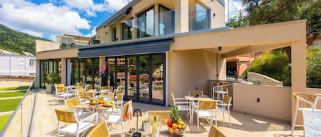 Un espace de restauration extérieur moderne, doté de tables et de chaises, d’une partie fermée par des parois de verre et offrant une vue sur le paysage environnant.