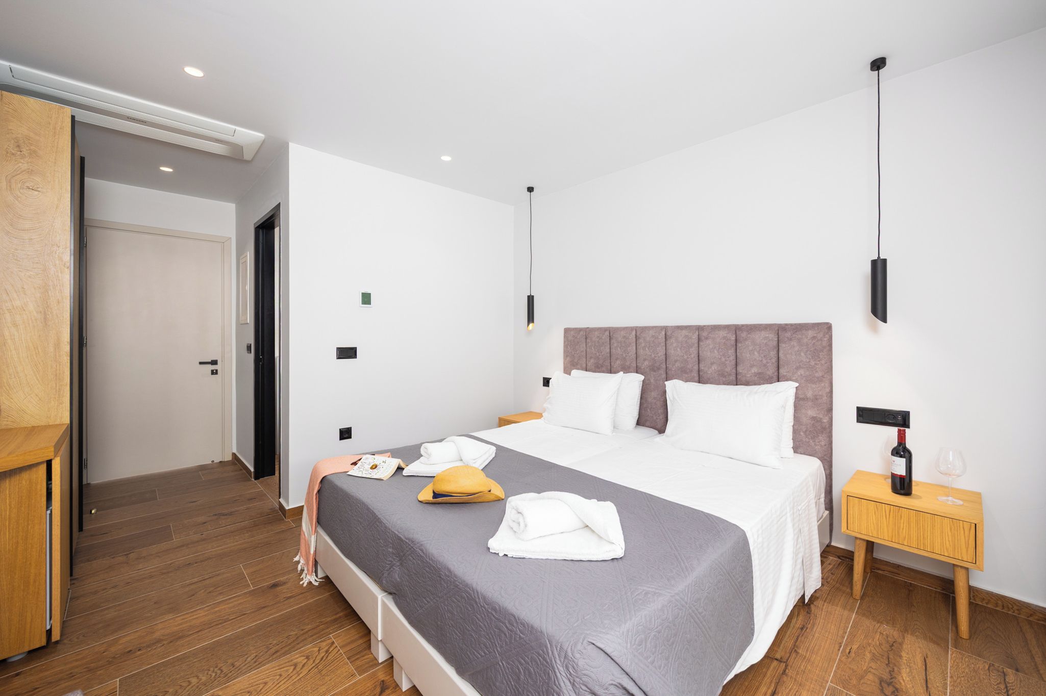 A modern hotel room with a large bed, a wooden nightstand, and a built-in wardrobe.