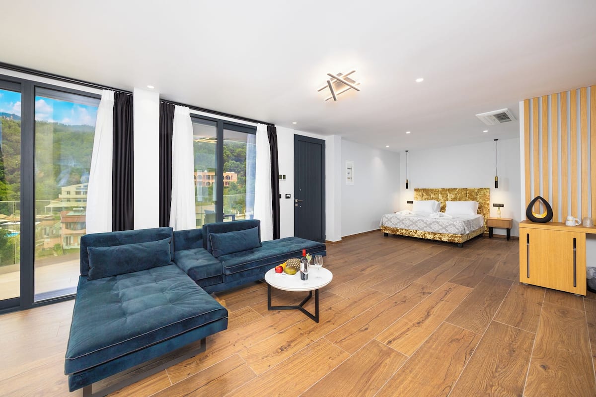 A modern living room with a blue sofa, a round coffee table, and a bed with a gold headboard.