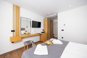 Une chambre d’hôtel moderne équipée d’un lit, d’une coiffeuse avec un miroir, d’une télévision et d’une armoire en bois.
