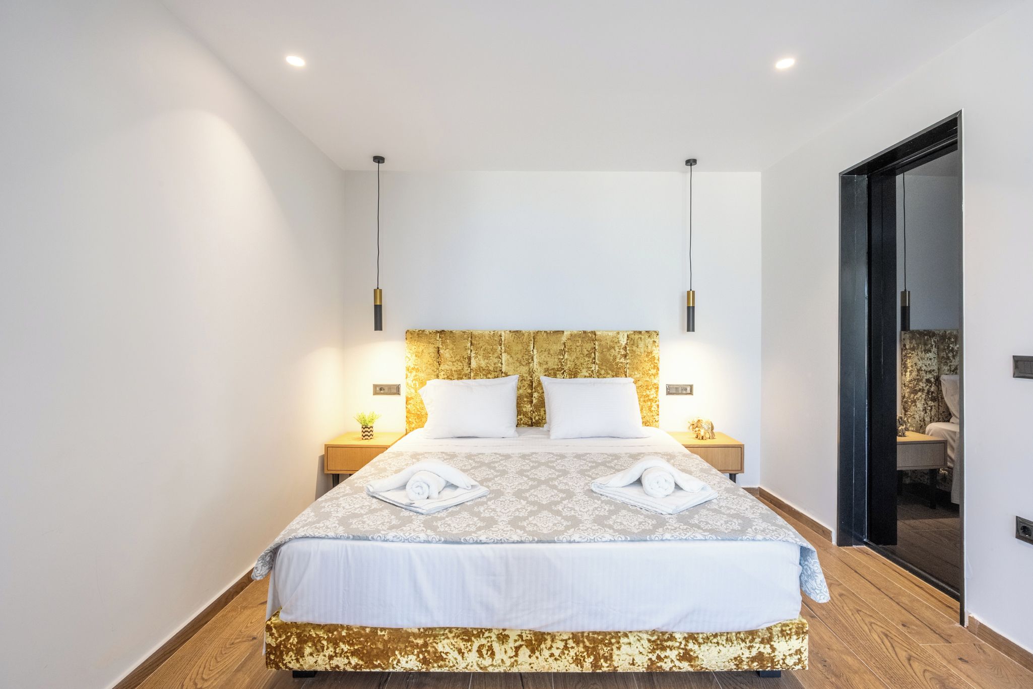 A modern hotel room with a large bed, wooden flooring, and a gold-patterned headboard.