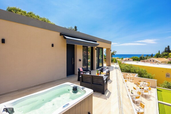 A modern outdoor terrace with a hot tub, seating area, and a view of the sea. - Nobile Hotel (Corfu)