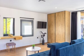 A modern living room with a blue sofa set, a small round table, a wooden cabinet, and a TV mounted on the wall. - Nobile Hotel (Corfu)