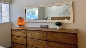 A modern room with a large mirror, a wooden dresser, a potted plant, and a decorative sign. - Modern Condo in Old Village (Mammoth Lakes)
