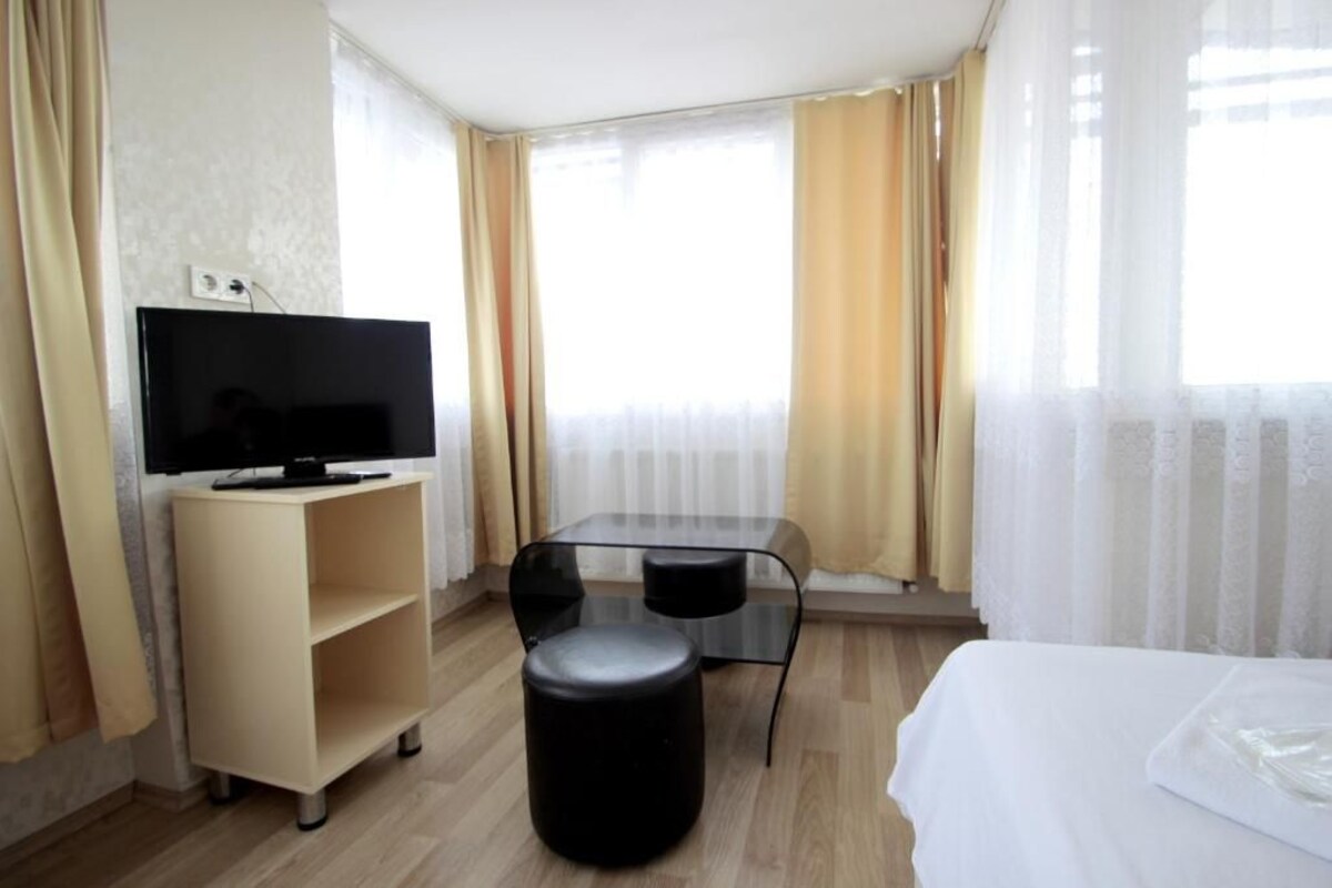 A hotel room with a bed, a TV on a stand, a small table, and a chair.