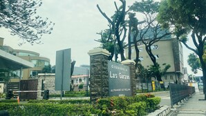 A sign for Ciudadela Las Garzas with a modern building in the background.