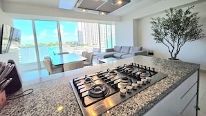 A modern kitchen with a gas stove, granite countertop, and a view of a balcony with a pool. - Marea condo vista espectacular 4pax (Cancun)