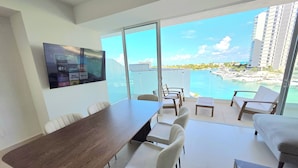 A modern hotel room with a balcony, a dining area, and a TV screen displaying various channels. - Marea condo vista espectacular 4pax (Cancun)