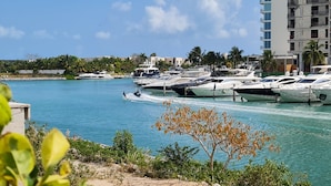 A marina with multiple yachts docked, a clear blue sky, and a coastal building in the background. - Marea condo vista espectacular 4pax (Cancun)