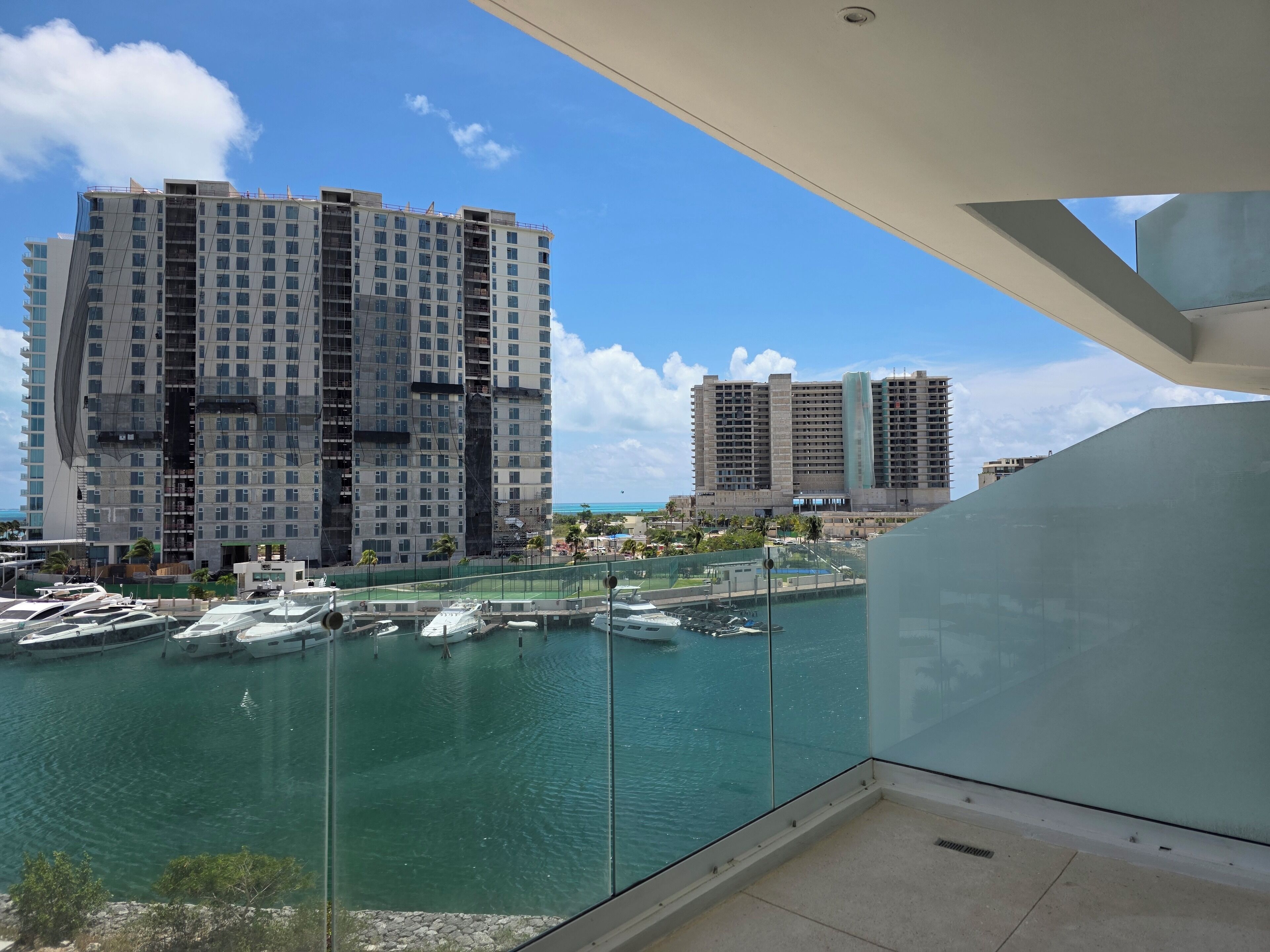 A view of a marina with boats docked, a large building with multiple floors, and a clear blue sky.